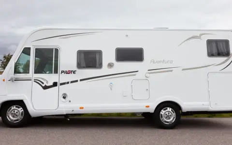 Vit husbil, Pilote G740 Aventura, parkerad vid en väg med gräs och träd i bakgrunden.