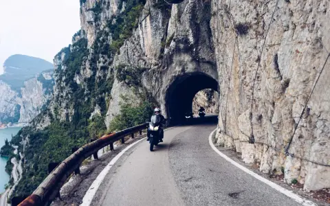 Motocykliści przemierzają malowniczą strada della forra, wjeżdżając w skalny tunel. Widok na jezioro i góry zapiera dech.