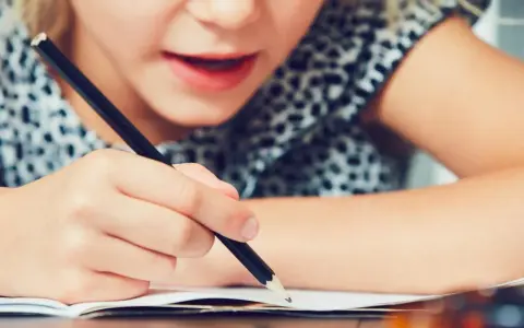 Dziecko zmagające się z pisaniem, co może być oznaką dysleksji. Skupienie na twarzy i ręce trzymającej ołówek.