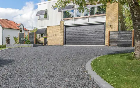 En vacker uppfart med mörkt grus leder fram till ett modernt hus med garageport.