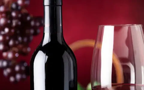 Bouteille de vin rouge connu, verre à vin et grappe de raisins sur fond rouge.