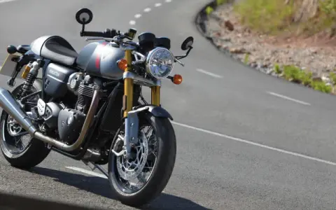 Srebrny Triumph Thruxton 900 na krętej drodze, gotowy na triumfalną jazdę.