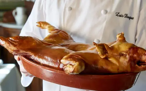 Cochinillo asado, un clásico que comer en Segovia. Un chef presenta este manjar dorado en una cazuela.
