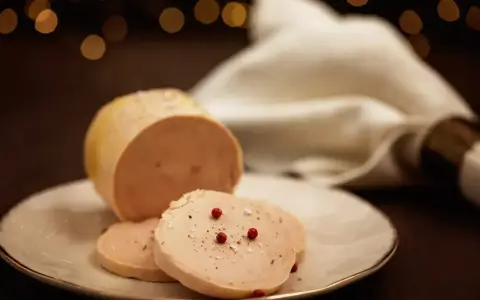 Tranche de foie gras, une des spécialités culinaires Dordogne, assaisonnée de poivre et de baies roses sur une assiette blanche.