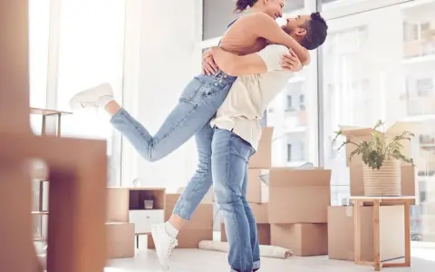 Glückliches Paar umarmt sich in einem neuen Zuhause voller Umzugskartons. Ein aufregender Moment, wann zusammenziehen!