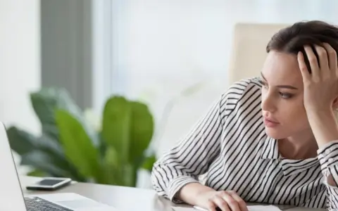 En kvinna sitter vid ett skrivbord, ser ut att vara omotiverad på jobbet. Hon vilar huvudet i handen och tittar tomt framför sig.