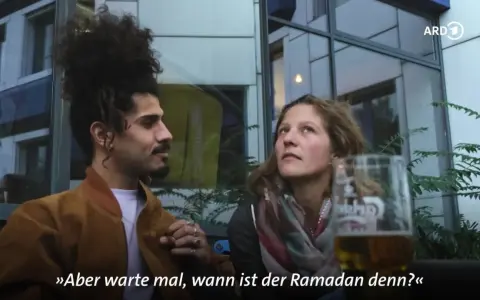 Ein Mann mit vollem Haar und eine Frau sprechen. Er fragt: "Aber warte mal, wann ist der Ramadan denn?" Die Fastenzeit im Islam ist ein wichtiges Thema.