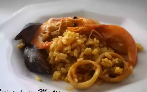 Arroz meloso con langostinos, mejillones y calamares en un plato blanco.
