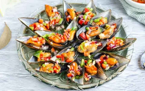 Mejillones a la vinagreta, frescos y coloridos, servidos en su concha con una picada de pimientos y cebolla.