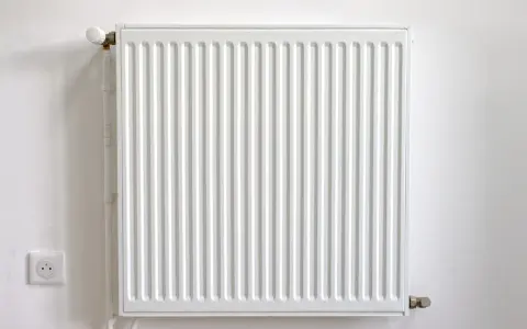 Radiador blanco con termostato, junto a un enchufe. Podría estar haciendo ruido radiador.