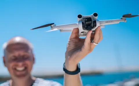 Ręka trzyma drona DJI Mini 3 Pro, gotowego do lotu. Jego imponujący zasięg pozwoli na uchwycenie niesamowitych ujęć.