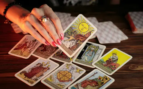 Dłoń z pierścionkiem wybiera kartę Słońce z talii tarot. Rozłożony krzyż celtycki tarot zapowiada przyszłość.