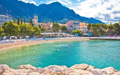 Słoneczna plaża w Baška Voda, z turkusową wodą i górami w tle. Idealne miejsce na relaks i odkrywanie atrakcji.