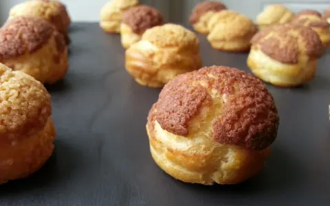 Une rangée de choux craquelins dorés et croustillants, certains avec un dessus brun, prêts à être dégustés.