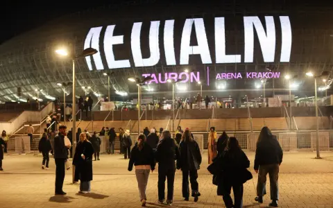 Tłum ludzi zmierza do Tauron Areny Kraków na koncert. Wielki napis na dachu obiektu zapowiada wydarzenie. To prawdziwy **rush w Polsce**!