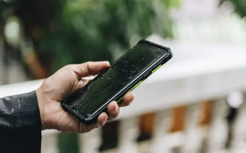 Dłoń trzyma mokry smartfon. IPX4 co oznacza? Ochronę przed zachlapaniem, idealny na deszcz.