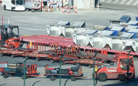 Röda lastbilar och vagnar med bagage på en solig yta vid teneriffa flygplats. En gaffeltruck står redo.
