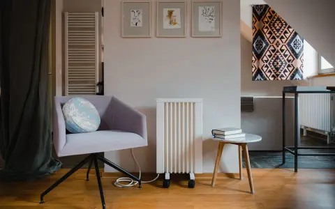 Un fauteuil confortable, un radiateur rayonnant blanc et une petite table avec des livres créent un coin lecture cosy.