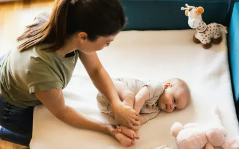 Mama bawi się z 3 miesięcznym dzieckiem, delikatnie masując jego stópki. Obok leżą pluszowe zabawki.