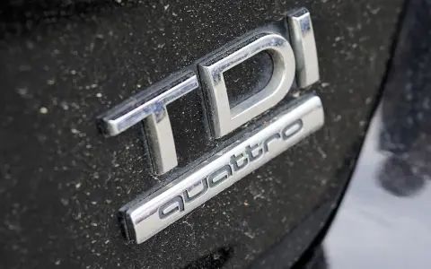 Emblematy TDI i Quattro na zakurzonym czarnym lakierze samochodu.