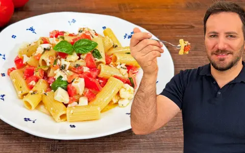 Un uomo sorride mentre assaggia una forchettata di pasta alla checca, un piatto fresco con pomodori, mozzarella e basilico.