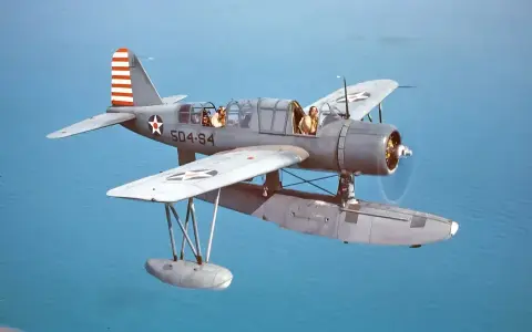 Ein Wasserflugzeug mit zwei Piloten fliegt über das Meer. Die Markierungen auf dem Flugzeug sind die von siai Marchetti.