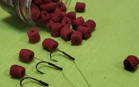 Czerwone kulki zanętowe i haczyki wędkarskie. Różne rozmiary haczyków wędkarskich i kulek.
