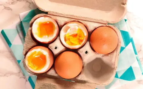 Uova alla coque in un cartone, alcune aperte mostrano tuorli dorati e cremosi, pronte per essere gustate.