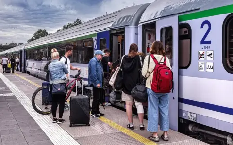 Ludzie z bagażami i rowerem czekają na pociąg PKP na peronie.