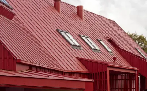 Rött, bandat plåttak med flera takfönster och skorstenar. Ett modernt hus med en slående takkonstruktion.