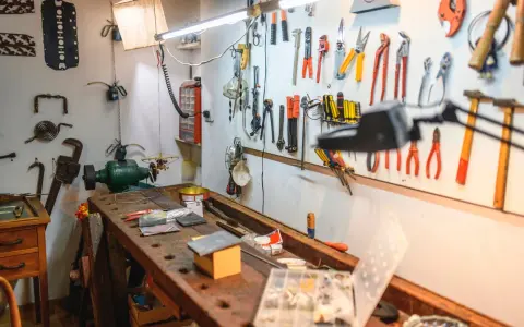 Wszystkie narzędzia wiszą na ścianie, gotowe do użycia w domowym warsztacie majsterkowicza. Na ławie leżą drobne przedmioty.