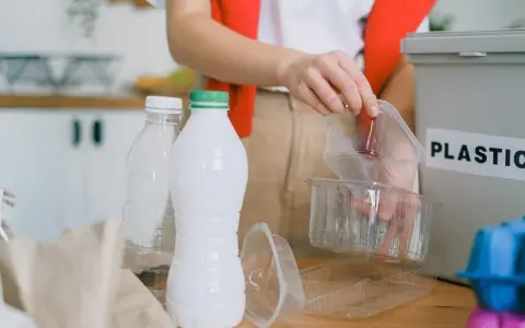 Segregacja odpadów to pierwszy krok, jak ograniczyć plastik. Ręka wrzuca plastikowe opakowania do pojemnika z napisem "PLASTIC".