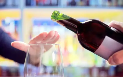 Hand stoppt Weinglas, während eine Flasche Rotwein eingegossen wird. Ein Symbol für bewussten Weinkonsum weltweit.