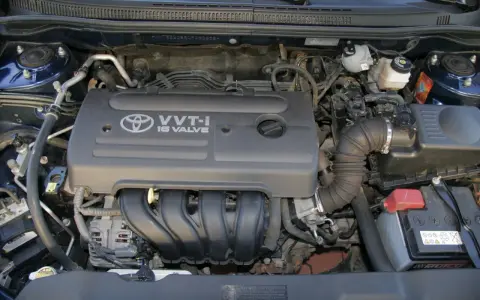 Silnik VVT-i 16 Valve z Toyoty Corolla E12. Widoczny alternator, akumulator i elementy układu dolotowego.