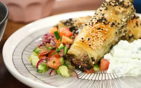 Krispiga filodegsrullar med sesamfrön, serverade med en fräsch tomatsallad och vitlökssås. Ett utsökt burek recept!