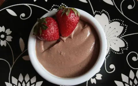 Délicieuse crème au chocolat onctueuse, garnie de deux fraises fraîches, servie dans un bol blanc sur une assiette noire décorée.