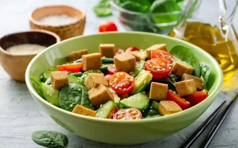 Pyszna sałatka z tofu, pomidorkami koktajlowymi, ogórkiem i szpinakiem, posypana sezamem. Idealna na lekki posiłek.