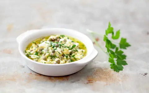 Sauce gribiche, une préparation maison à base d'œufs durs hachés, de câpres et de persil frais, dans un bol blanc.