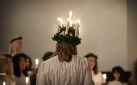 En flicka med ljuskrona bär fram ett lucia namn. Hon leder en procession av flickor med ljus i mörkret.