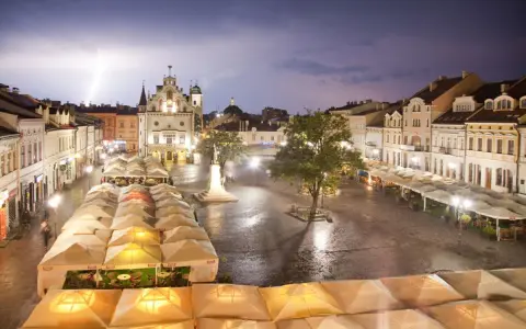 Nocny rzeszów rynek podczas burzy z piorunami. Mokry bruk, oświetlone kamienice i ogródki restauracyjne pod namiotami tworzą magiczny klimat.