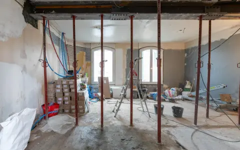 Chantiers : étais métalliques soutenant une poutre en cours de consolidation pour le prix d'une fondation maison. Matériaux et outils de construction visibles.