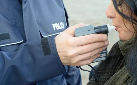 Policjant w mundurze z napisem "POLICJA" mierzy kobiecie poziom alkoholu alkomatem.