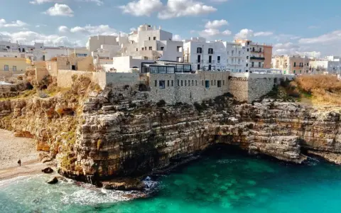 Scogliere mozzafiato e case bianche a picco sul mare turchese, perfetti **posti da visitare in Puglia estate**.