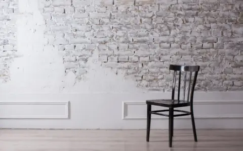 Silla negra frente a pared de ladrillo rústica, con un acabado de pintar pared de piedra en blanco que deja ver la textura original.