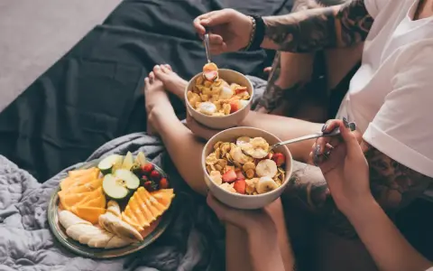 Para jedząca płatki z owocami i talerz świeżych owoców na łóżku. Zdrowy początek dnia, czyli zbilansowana dieta.