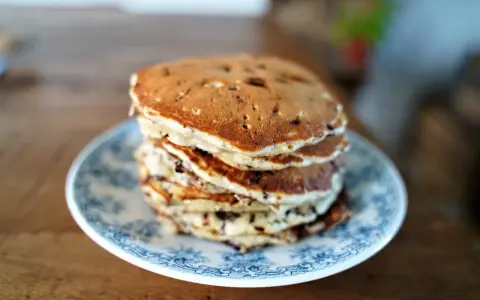 Pile de pancakes pepite chocolat sur une assiette bleue et blanche, prêts à être dégustés.