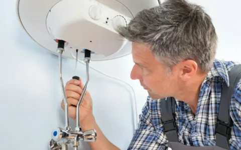 Mann mit Werkzeug am Warmwasserspeicher. Anleitung zum Warmwasserspeicher entkalken.