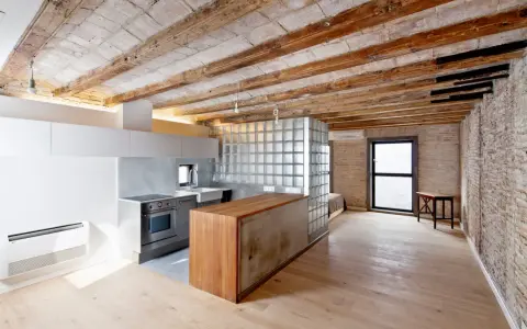 Cocina moderna con isla de madera y cristal, techos de vigas expuestas. Un espacio abierto que evoca la idea de como tirar un tabique para crear amplitud.