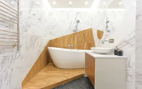 Salle de bain moderne avec baignoire îlot sur une estrade en bois, lavabo, miroir et carrelage marbre.