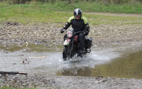 Motocyklista w kasku pokonuje wodną przeszkodę na kamienistej trasie w okolicach Jasła.